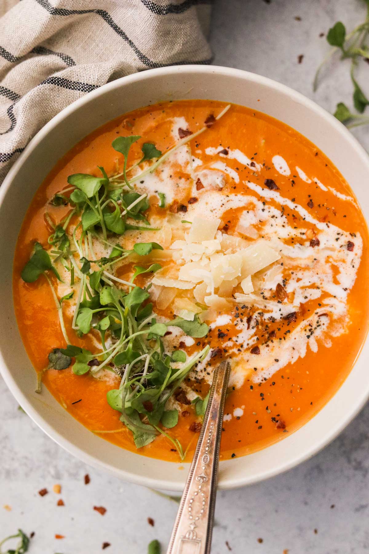 a white bowl filled with a creamy, blended soup and topped with pepper, parmesan cheese, and microgreens