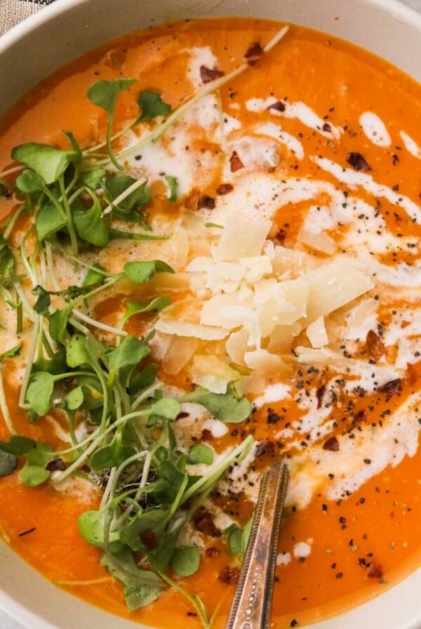 a closeup of creamy butternut squash soup with coconut milk topped with parmesan cheese, microgreens, and black pepper
