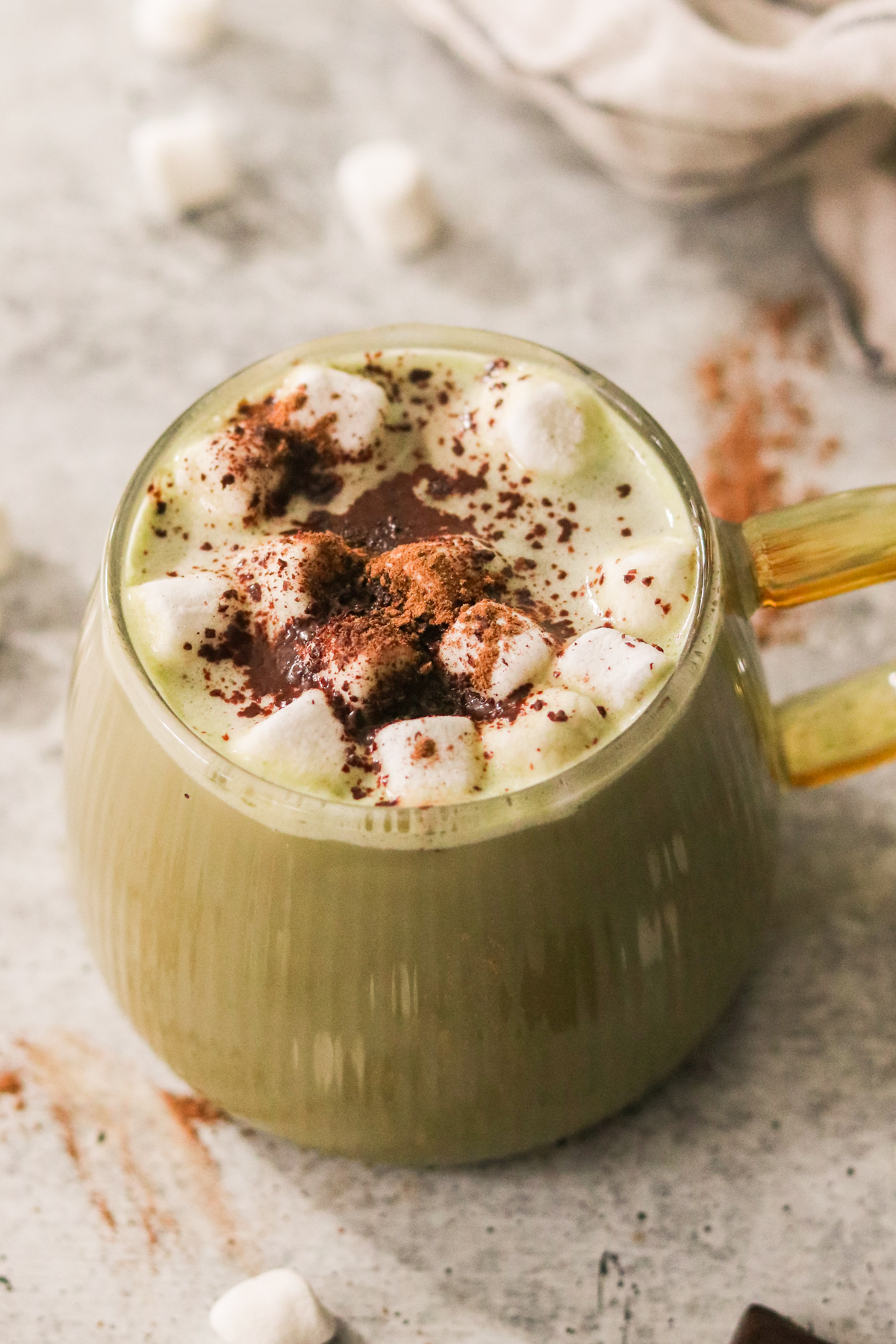 a glass mug filled with hot chocolate matcha and topped with marshmallows, and cinnamon