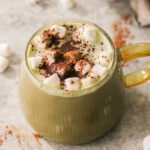 a glass mug of hot chocolate matcha latte topped with mini marshmallows and sprinkled with cinnamon