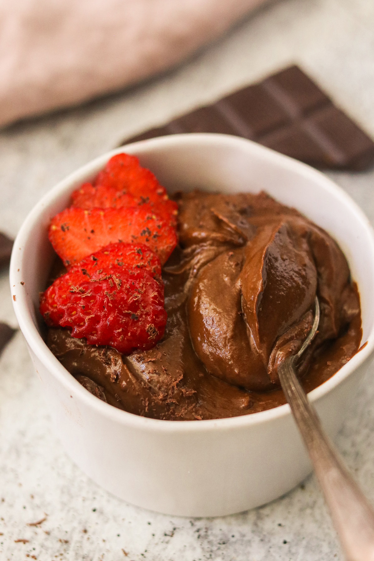 A small white bowl with sweet potato avocado chocolate pudding, topped with sliced strawberries and shaved chocolate
