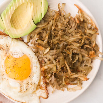 a white plate filled with avocado, egg, and air fryer hash browns.