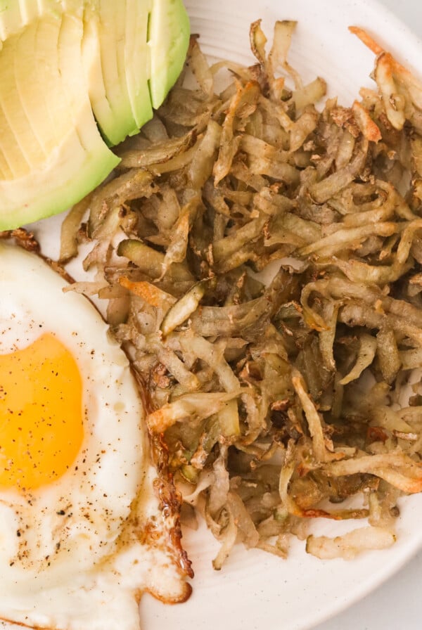 a white plate filled with avocado, egg, and air fryer hash browns.