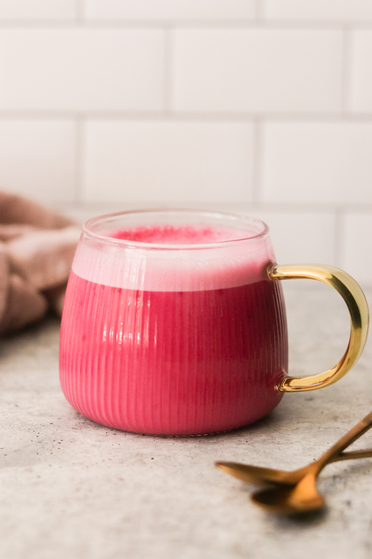 a glass mug with a gold handle filled with pink latte
