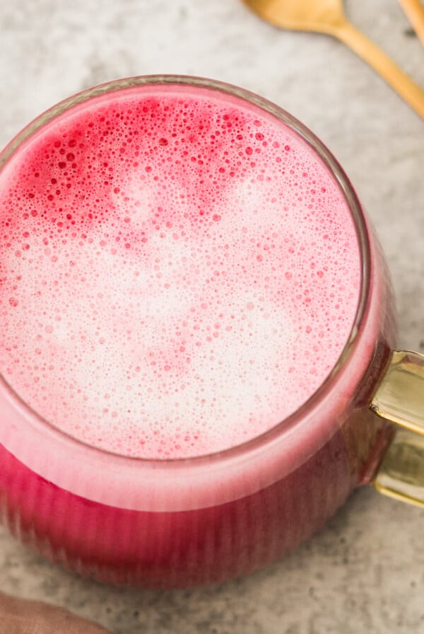an overhead shot of a pink latte in a glass mug with a gold handle