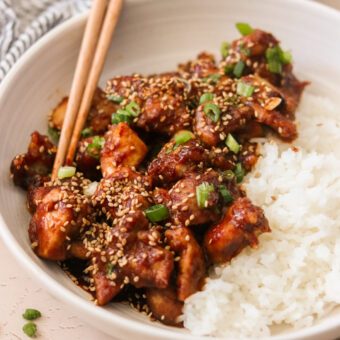 a plate of air fryer general tso's chicken on a plate with white rice and chopsticks resting on the side.