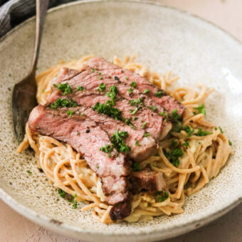 a close up of creamy pasta topped with slices of steak.