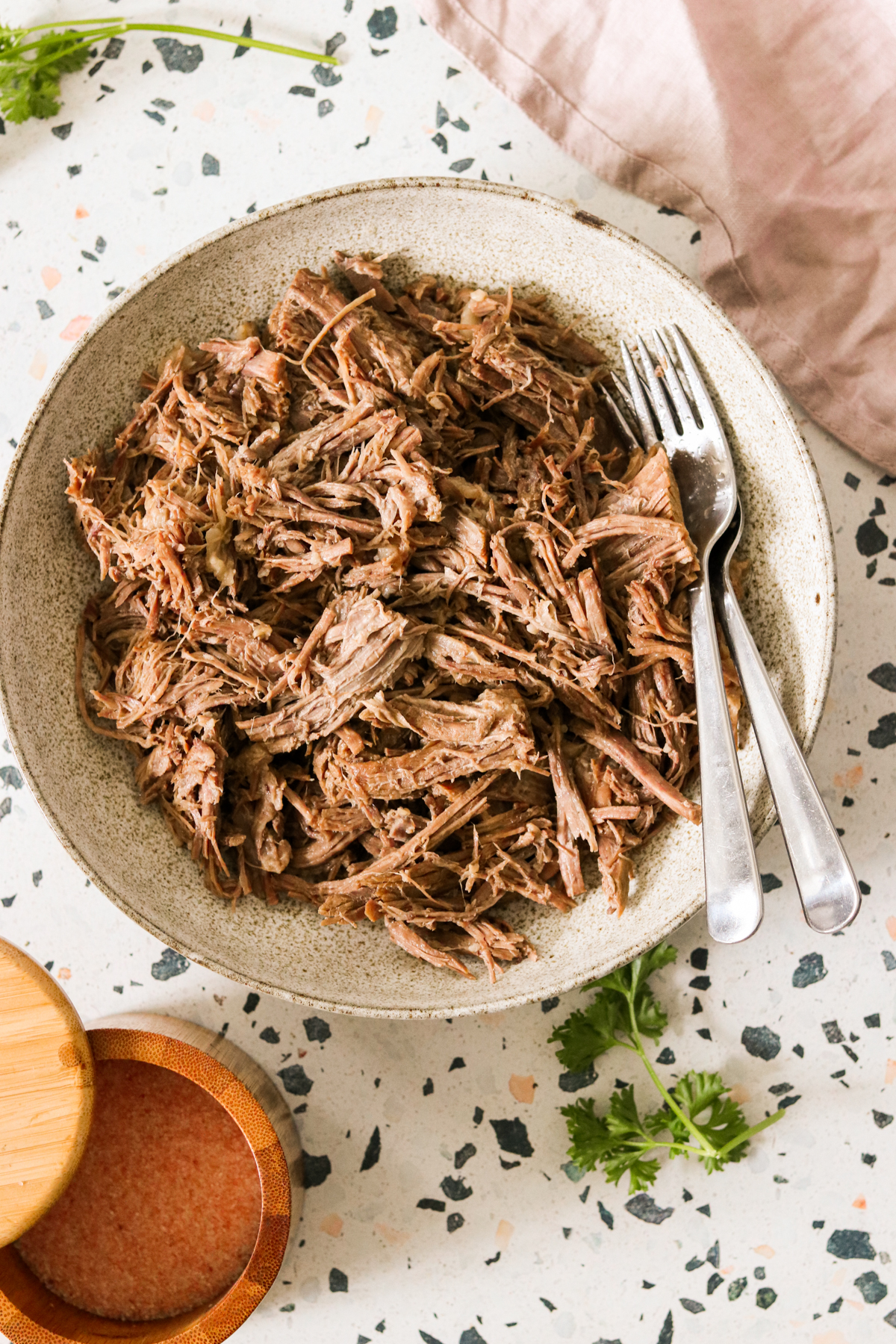 an overhead shot of shredded beef in a bowl with a silver fork resting on the side