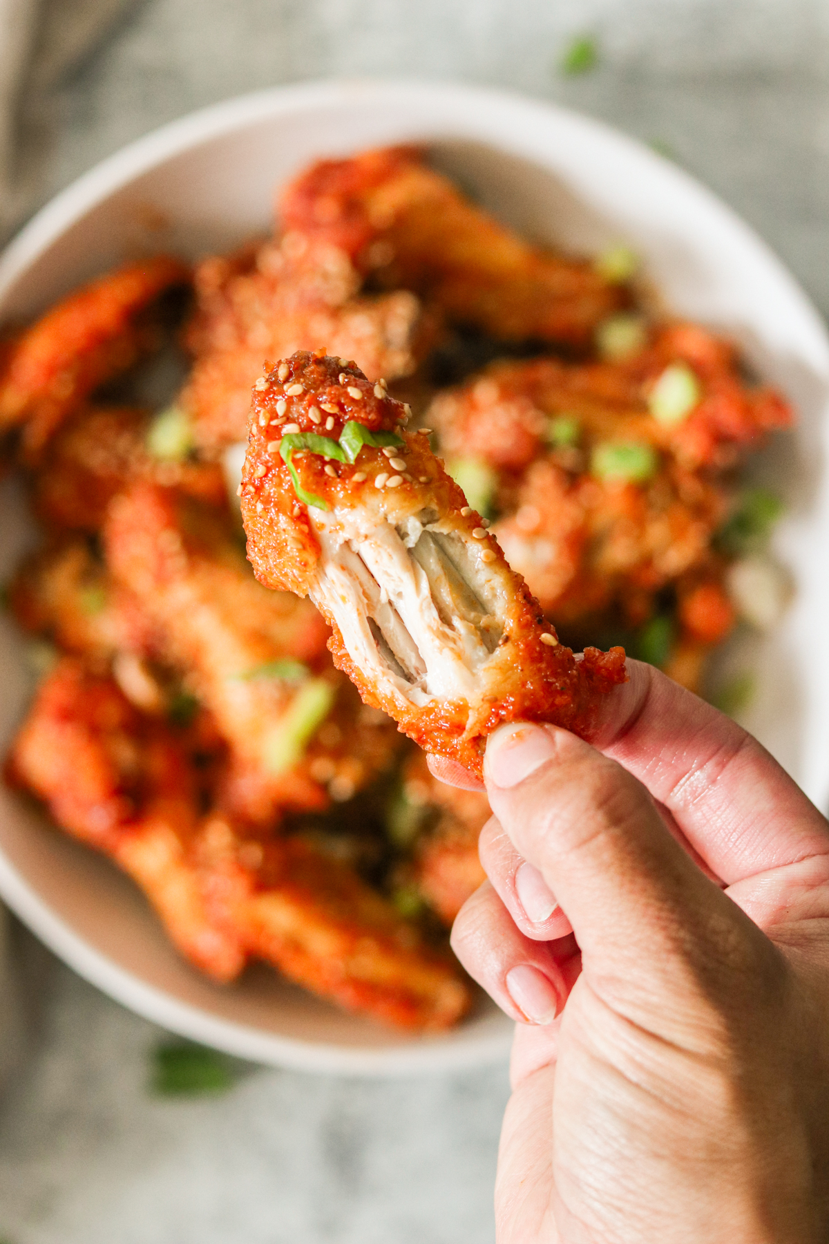 a hand holding an air fryer korean fried chicken wing with a bite taken out. 