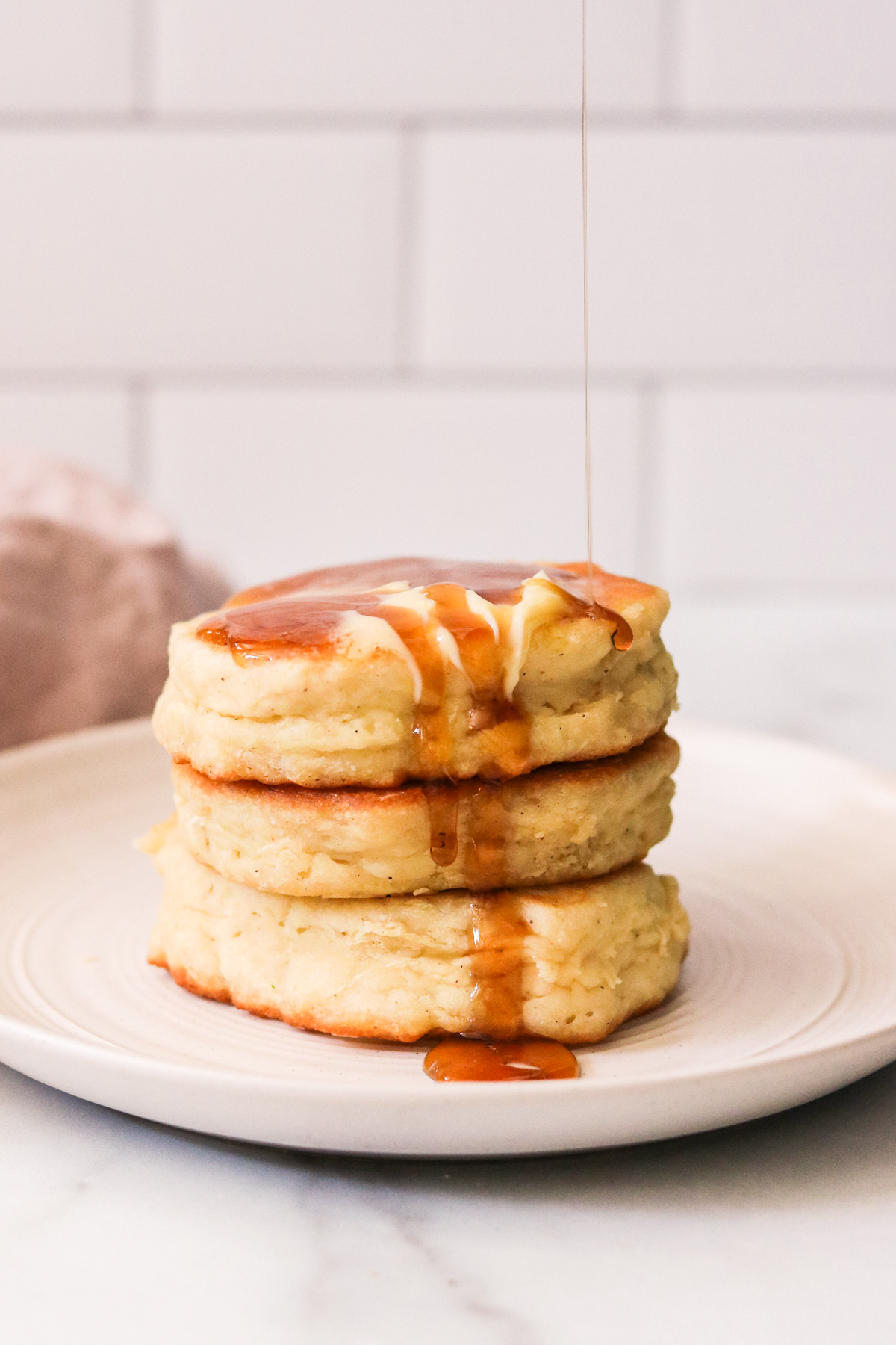 pouring syrup over a stack of eggless pancakes. 
