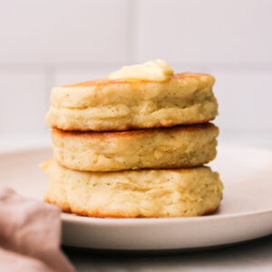 a stack of three fluffy eggless pancakes on a plate topped with butter and syrup