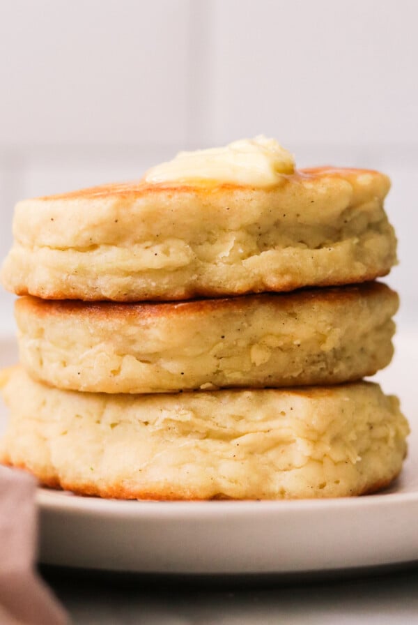 a stack of three fluffy eggless pancakes on a plate topped with butter and syrup