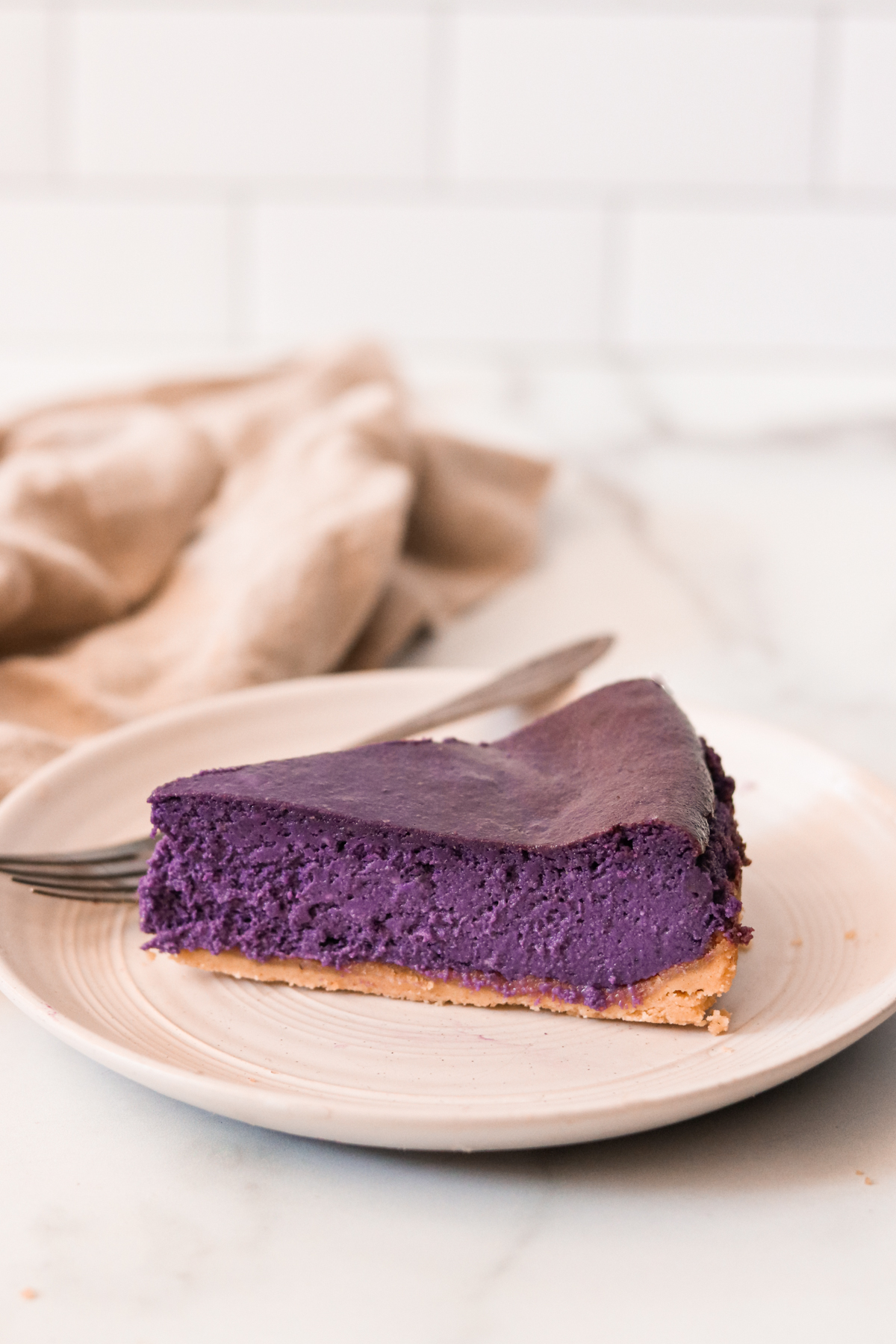 a slice of ube cheesecake on a white plate with a silver fork