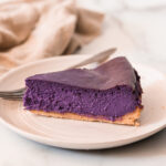 a slice of ube cheesecake on a white plate with a silver fork