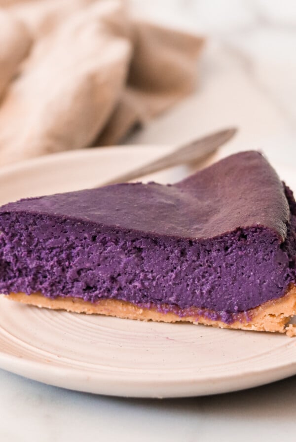 a slice of ube cheesecake on a white plate with a silver fork