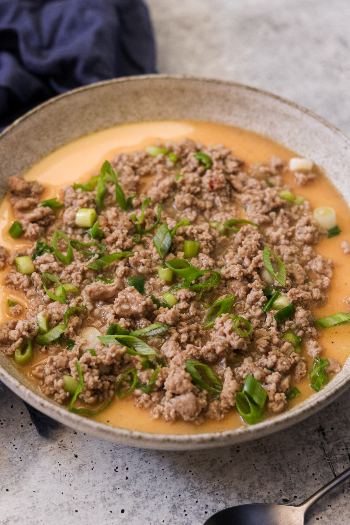 a bowl of Chinese steamed egg topped with ground pork and chopped green onions