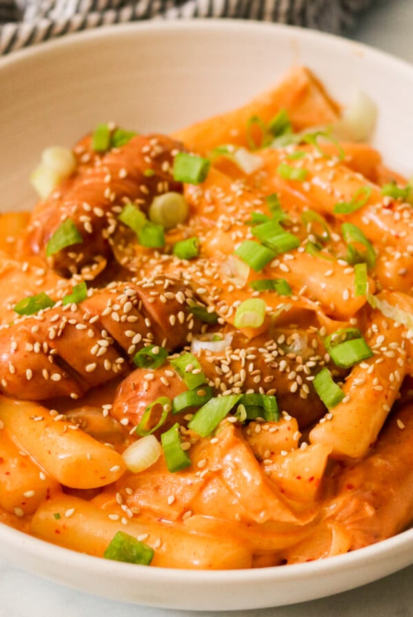 a bowl filled with rose tteokbokki and topped with sesame seeds and green onions