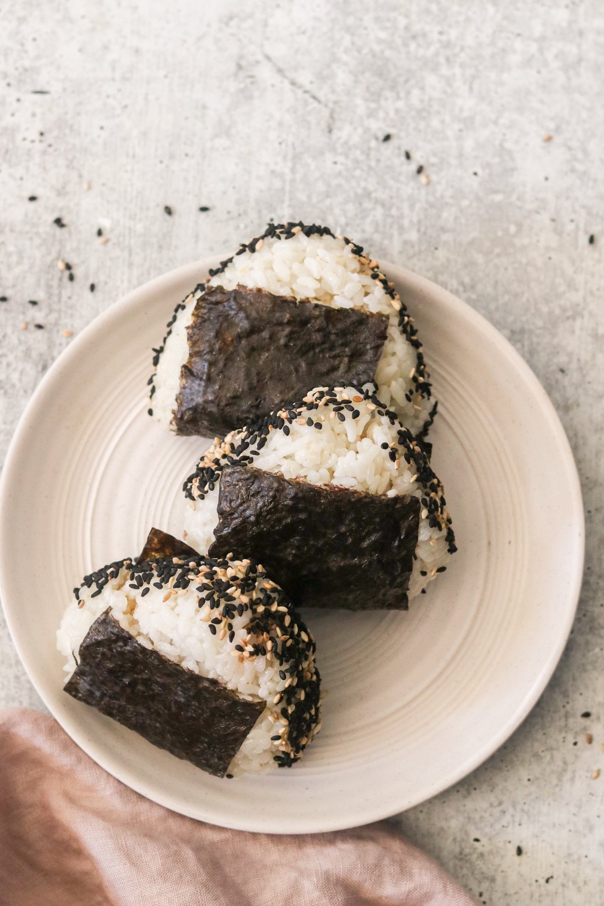 three tuna onigiri on a white plate topped with sesame seeds