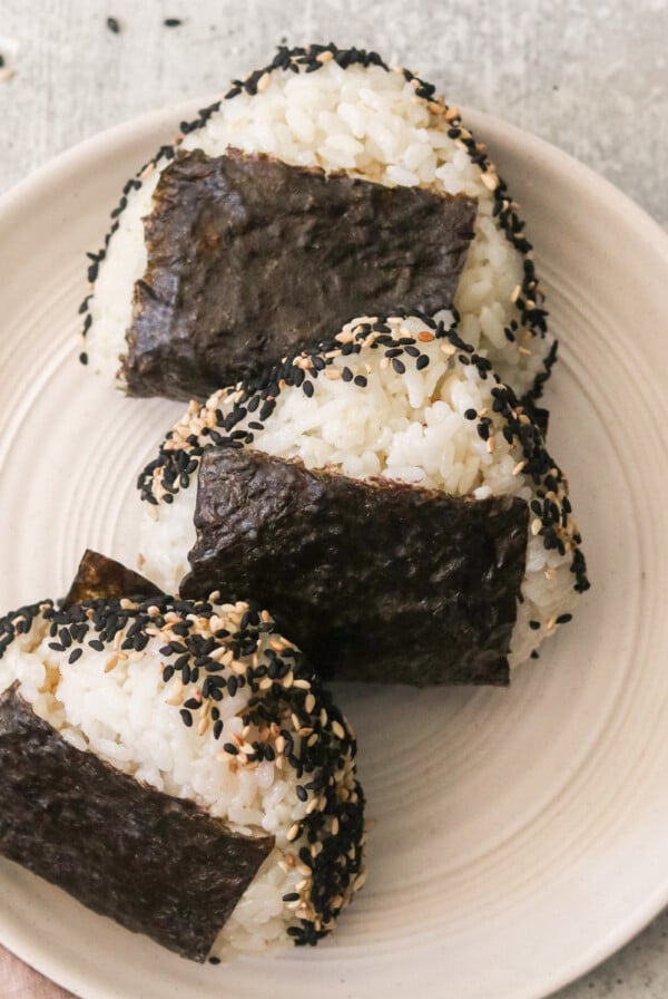three tuna onigiri on a white plate topped with sesame seeds