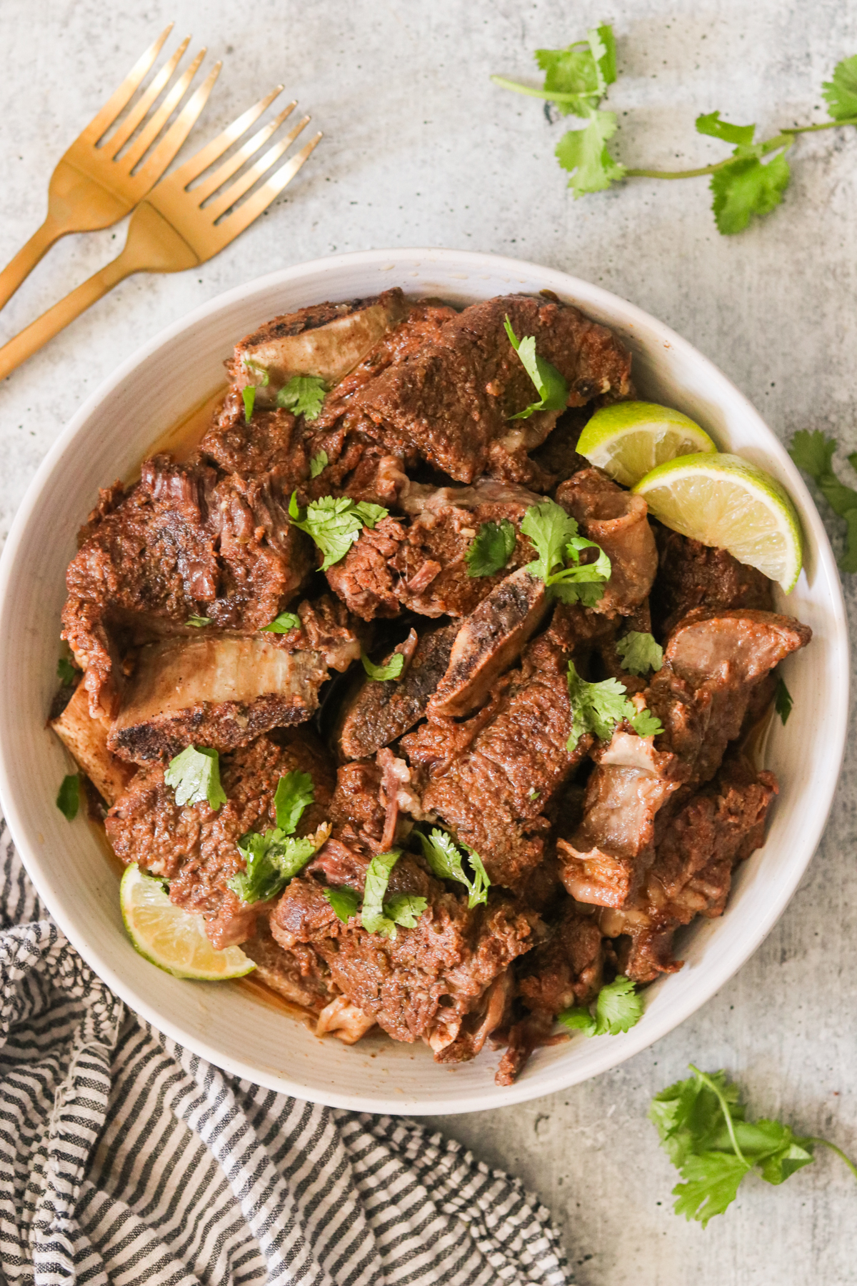 an overhead shot of instant pot short ribs in a white bowl topped with cilantro and lime wedges. 