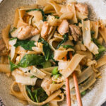 a plate of chicken pad see ew with chopsticks resting on the side