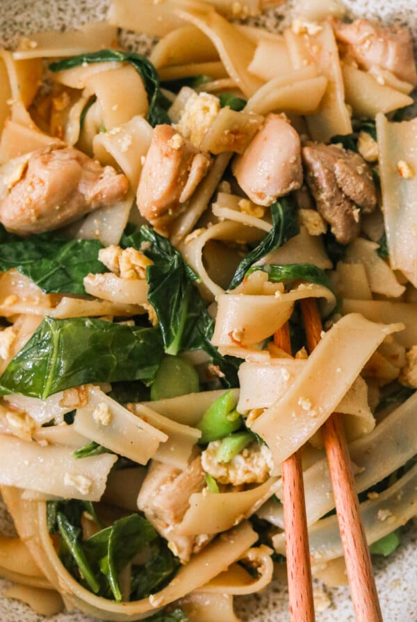a plate of chicken pad see ew with chopsticks resting on the side