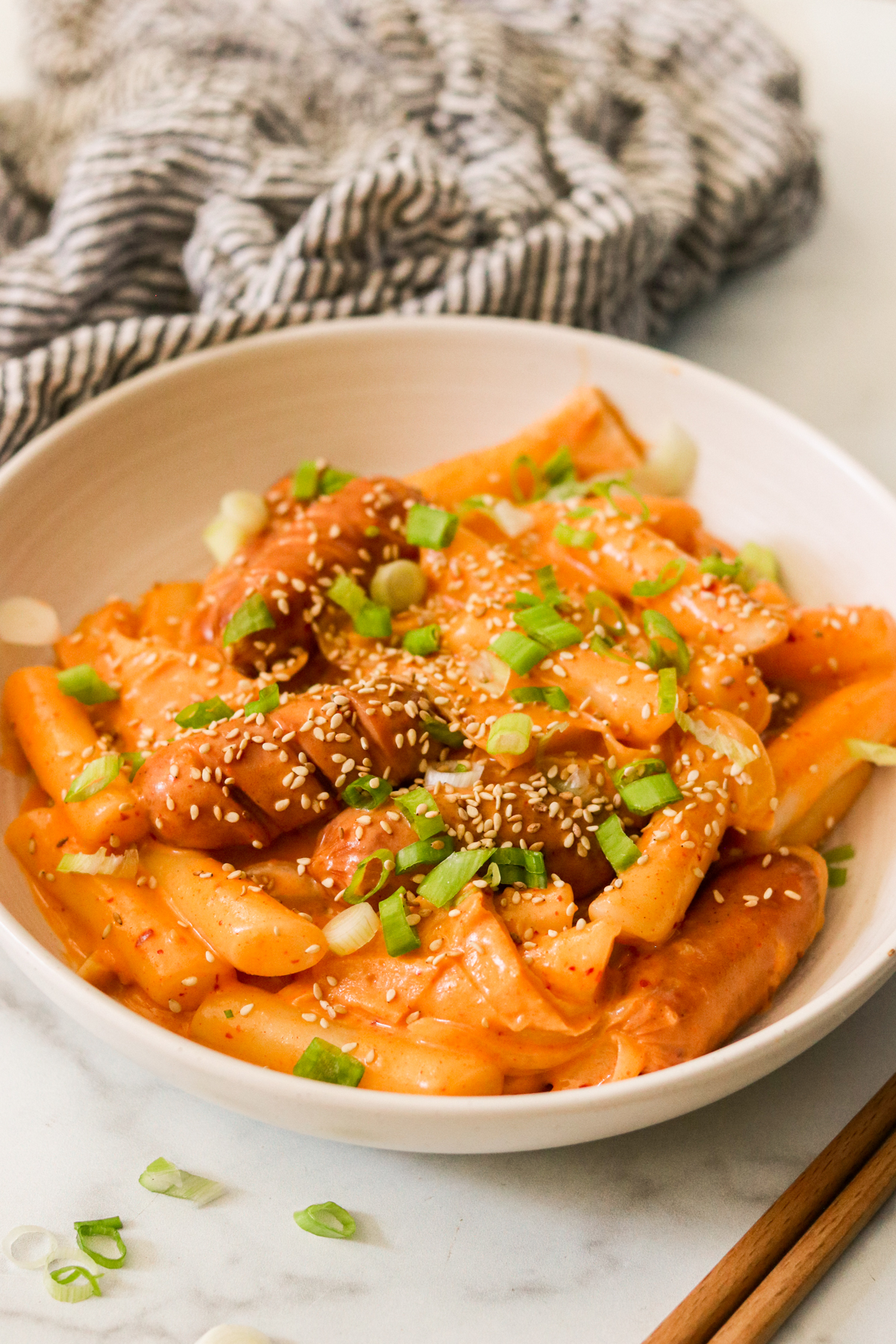 a bowl filled with rose tteokbokki and topped with sesame seeds and green onions