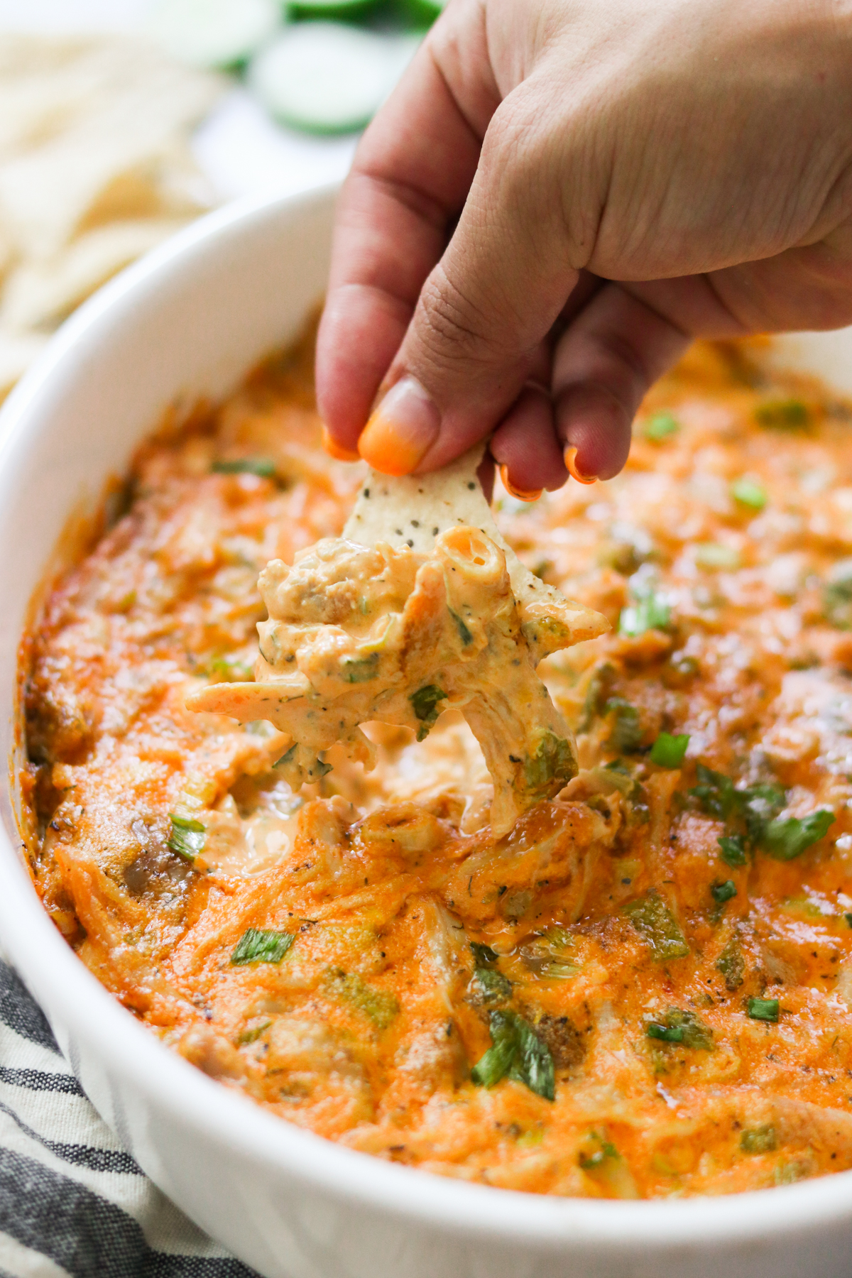a hand dipping a chip into a creamy, cheesy chicken dip