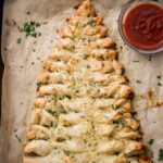 an overhead shot of Christmas tree bread on parchment paper with a small bowl of marinara sauce
