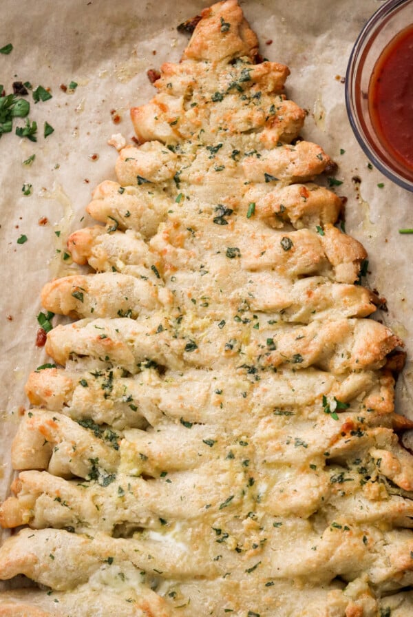 an overhead shot of Christmas tree bread on parchment paper with a small bowl of marinara sauce
