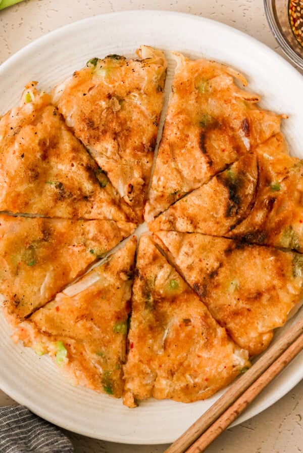 korean kimchi pancake on a white plate sliced into 8 triangles.