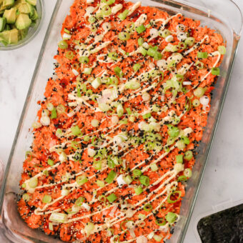 a salmon sushi bake in a casserole dish topped with mayo, sesame seeds, and green onions.