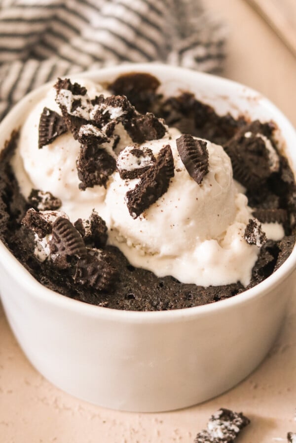 Oreo mug cake in a white ramekin, topped with vanilla ice cream and crushed cookies