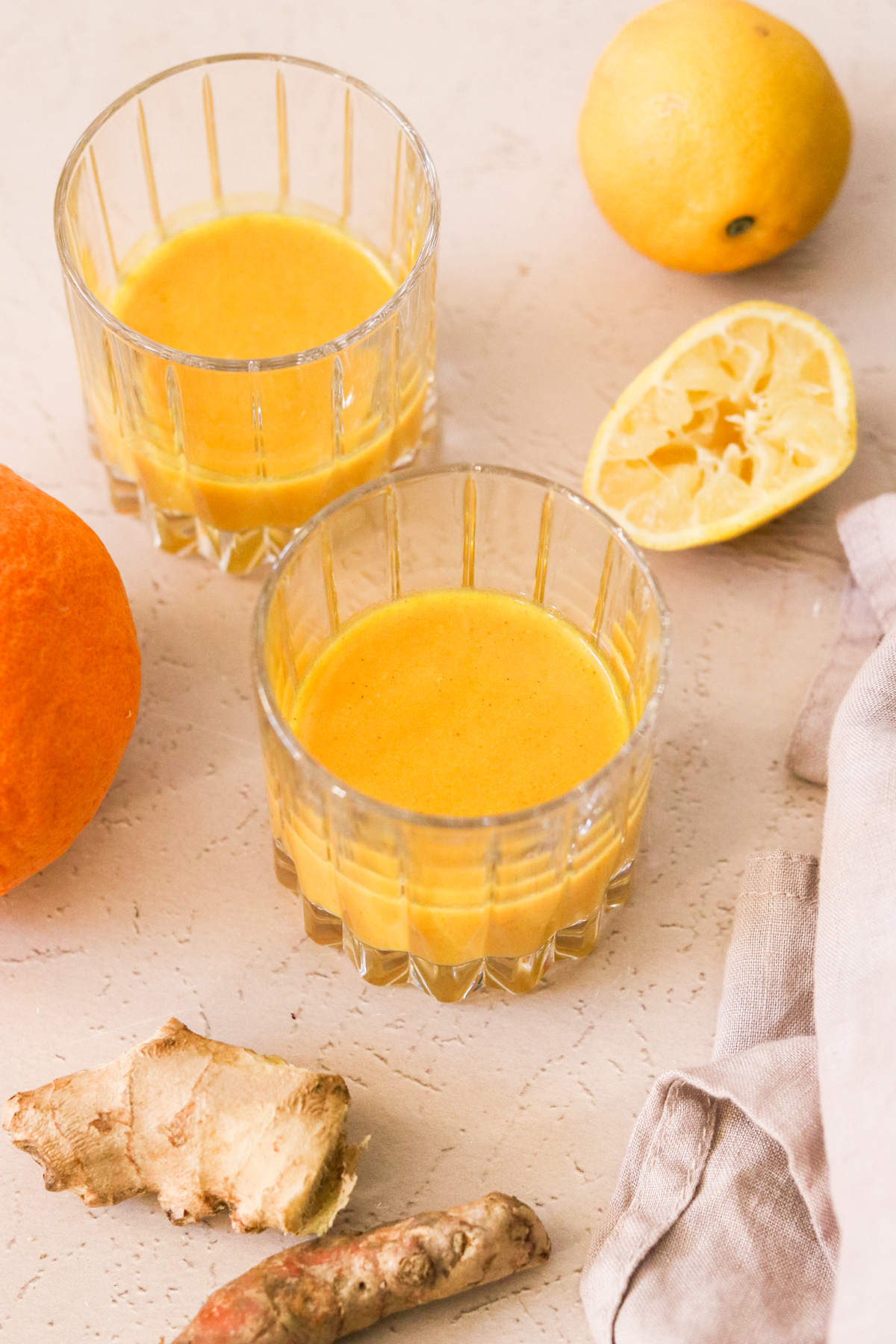 two glass filled with orange immunity shot recipe next to a squeezed lemon