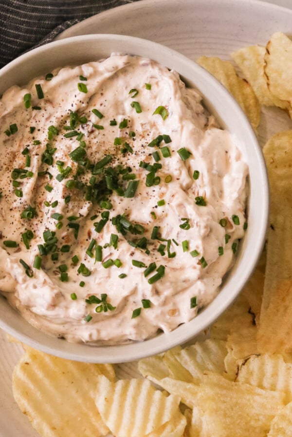 an overhead shot of greek yogurt french onion dip in a bowl on a plate next to potato chips
