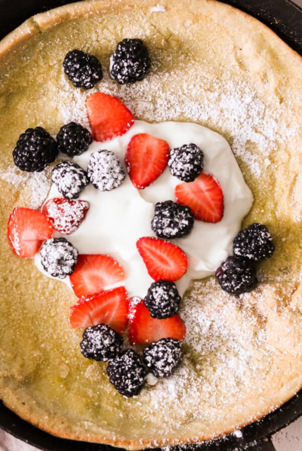 a gluten free dutch baby pancake in a cast iron pan topped with yogurt and berries
