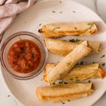 chicken taquitos on a plate next to a bowl of salsa