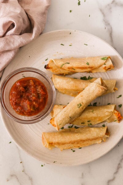 chicken taquitos on a plate next to a bowl of salsa