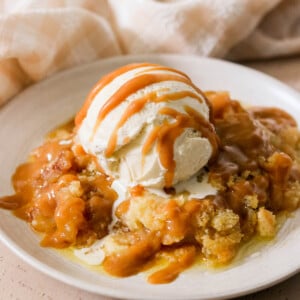 a slice if caramel apple dump cake on a plate topped with ice cream and caramel sauce.