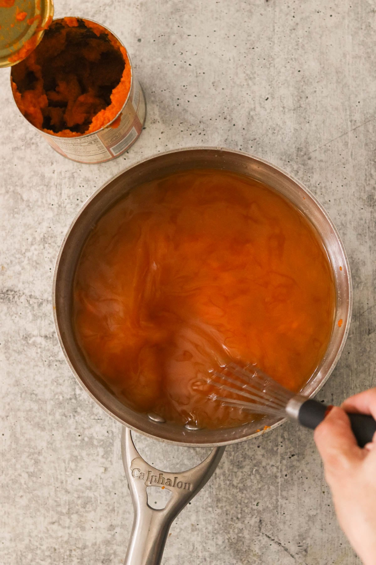 Pumpkin puree and broth in a saucepan being whisked.