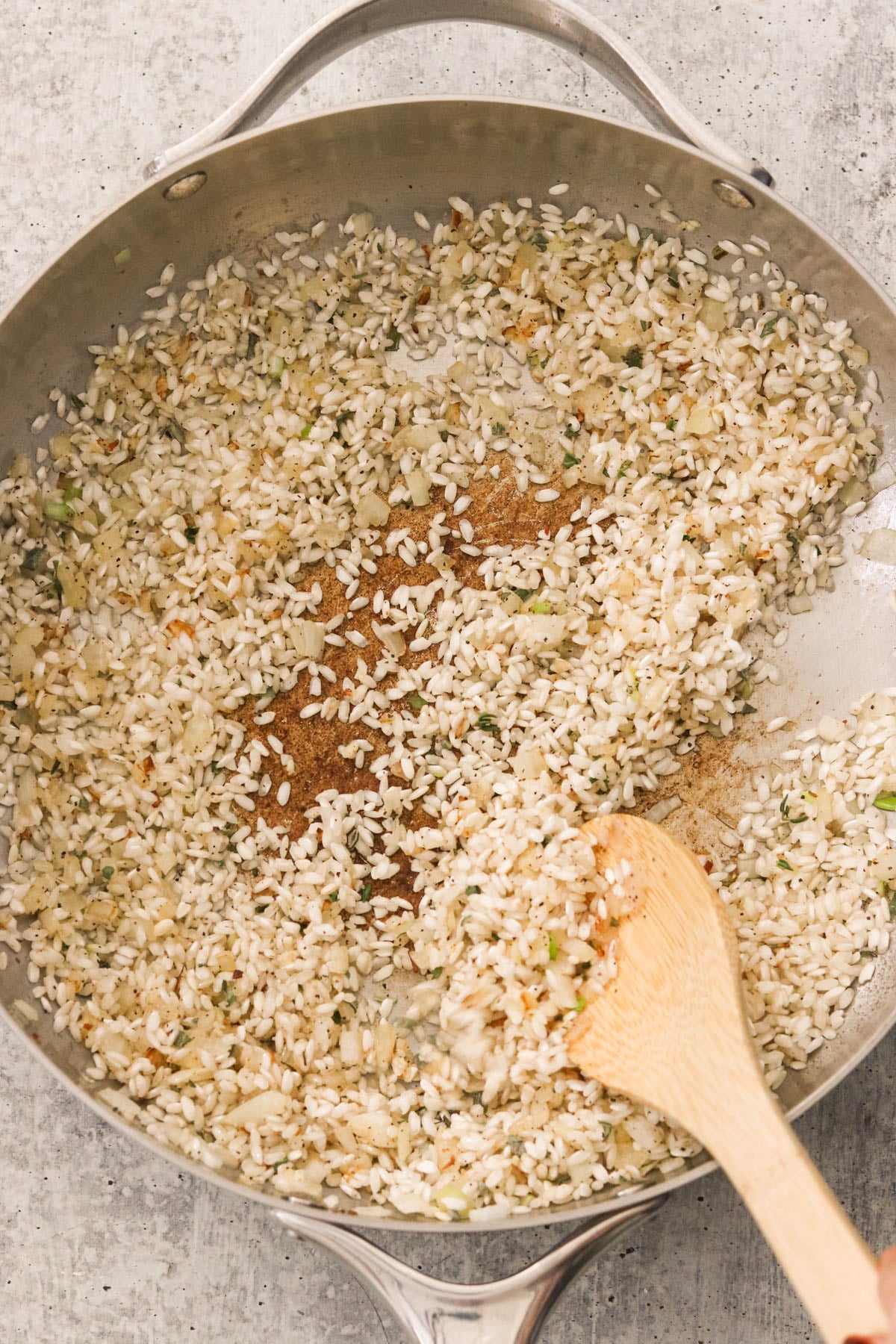 Arborio rice, sage, thyme, salt, and pepper cooking in a pan.