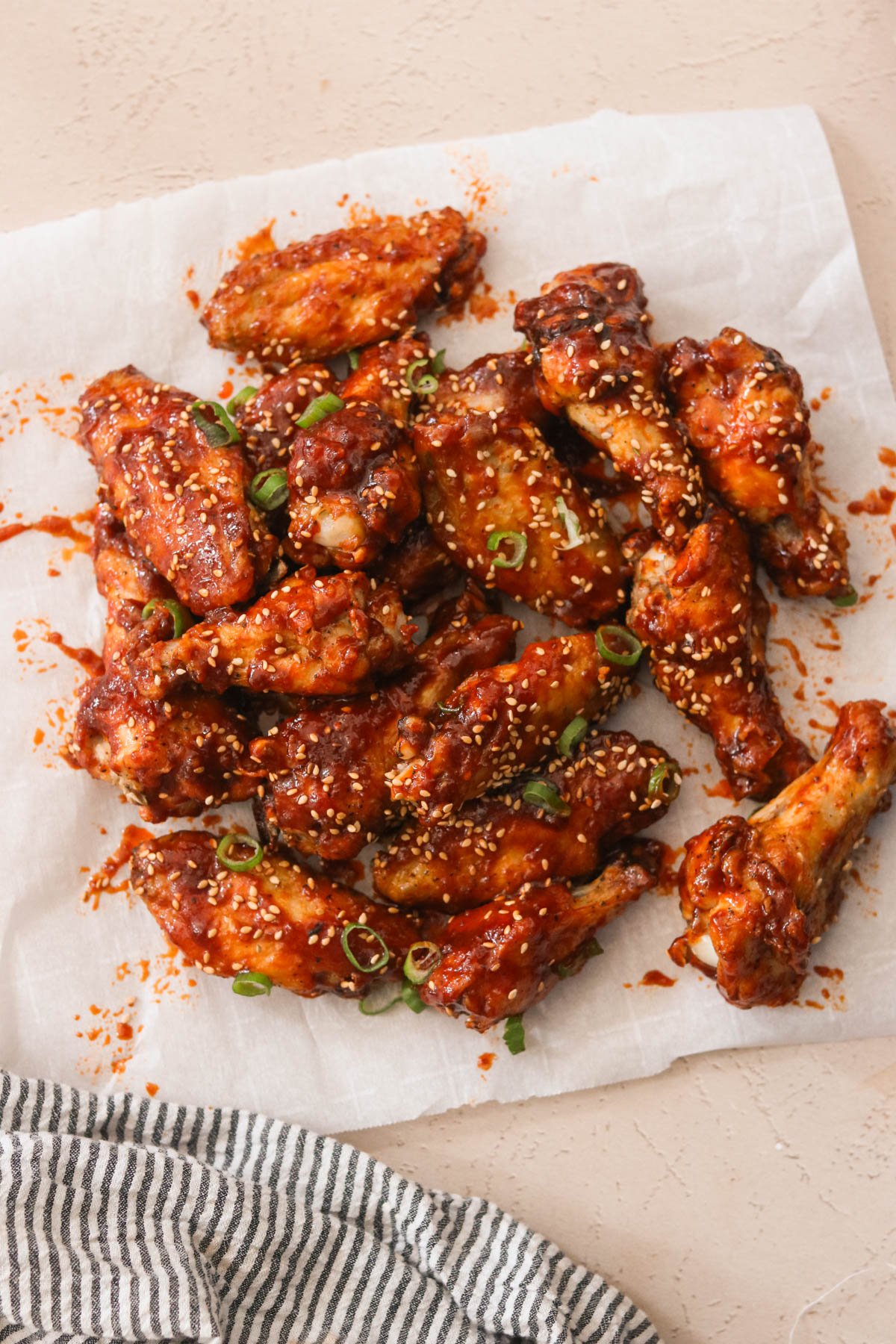 gochujang chicken wings on a piece of parchment paper and topped with scallions and sesame seeds 