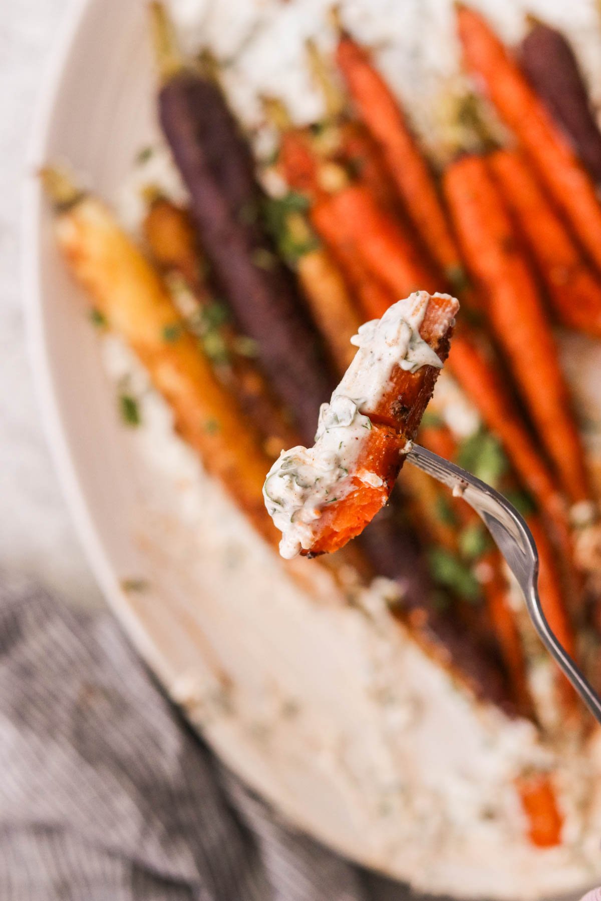 a fork holding a carrot dipped in yogurt sauce 