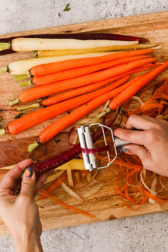 a hand peeling carrots with a veggie peeler 