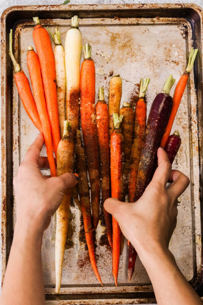 hands placing carrots on a sheet pan 