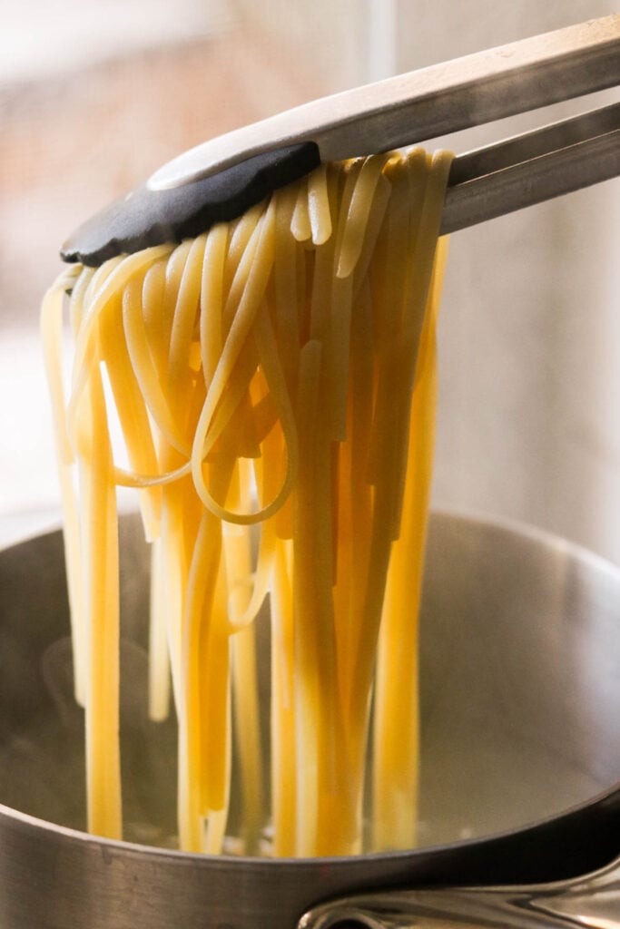 tongs pulling pasta out of boiling water 