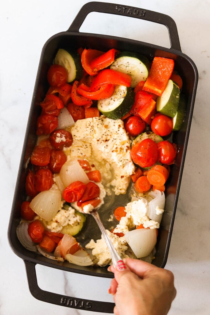 smashing the cooked veggies and feta cheese with a spoon 