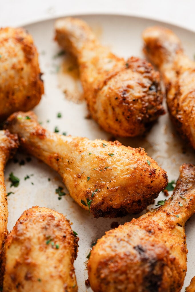 chicken drumsticks out of the air fryer on a a white serving plate