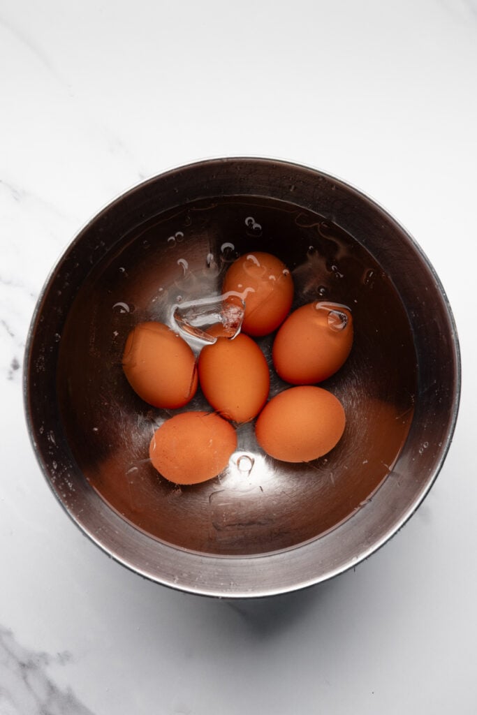 hard boiled eggs with shells on resting in a bowl of ice water