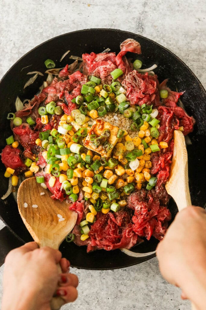 two hands mixing the dish with two wooden spoons 